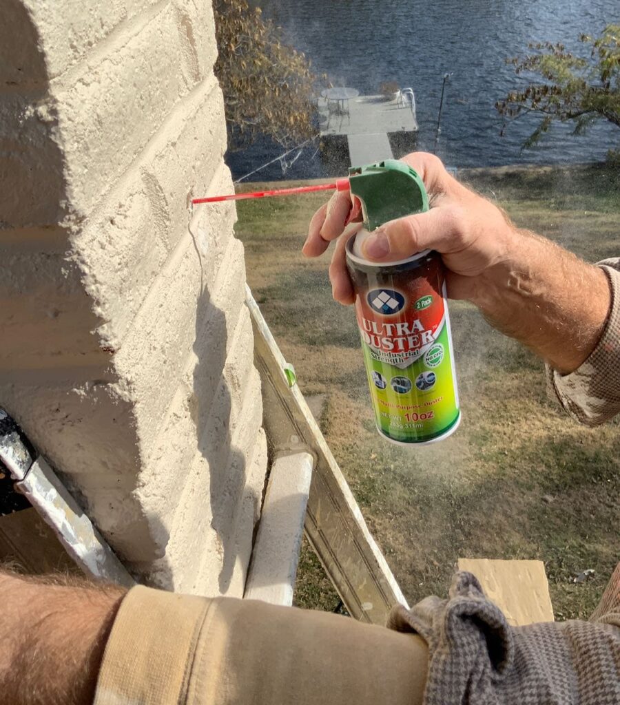 closeup of a can of compressed air blowing out the dust from the hole just drilled in the brick