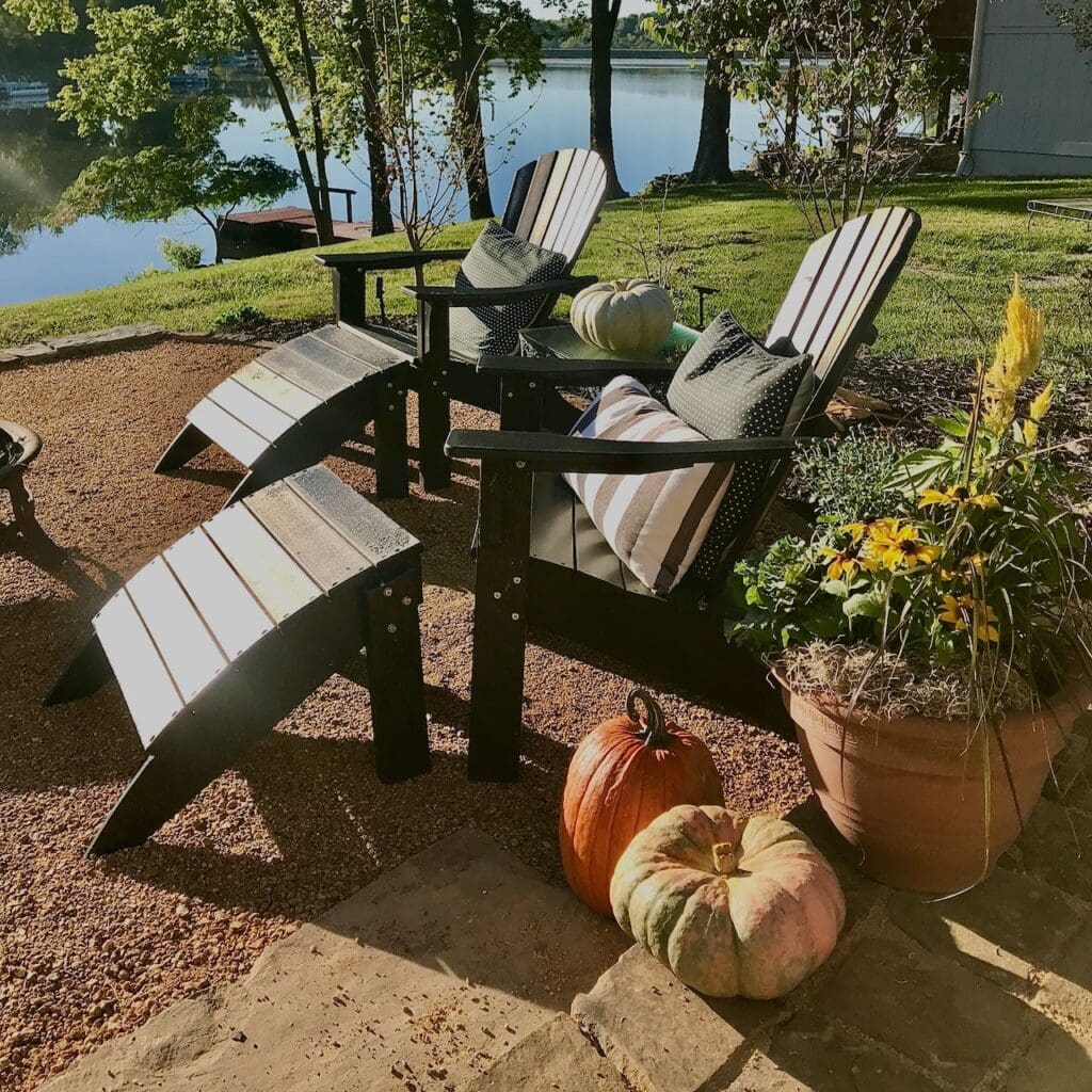 Two adirondack chairs with pillows and pumpkins and a large flower pot arrangement sitting on the finished DG patio