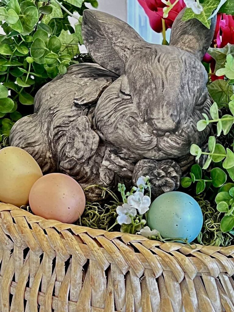 Closeup of bunny's face with three softtt-colored easter eggs close by , all nestled on a bed of dried moss overflowing a large basket