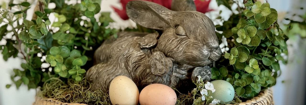 Wide title image of a concrete rabbit statue. surrounded with green vines and a few eggs