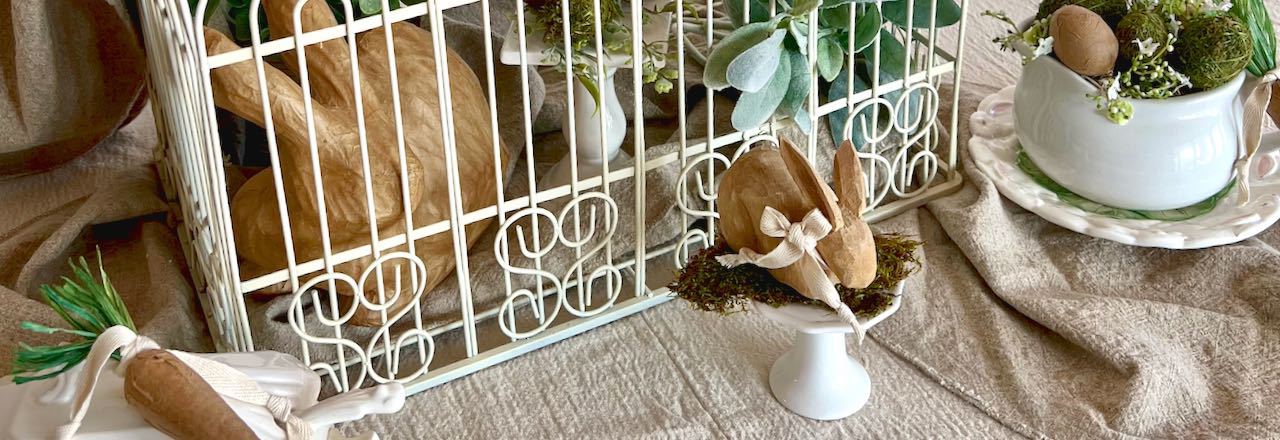 Wide closeup of bottom part of a large decorative birdcage decorated in neutrals and soft greens with bunnies, plants and eggs