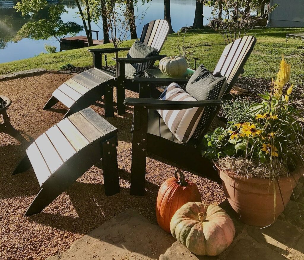 Two adirondack chairs with pillows and pumpkins and a large flower pot arrangement sitting on the finished DG patio