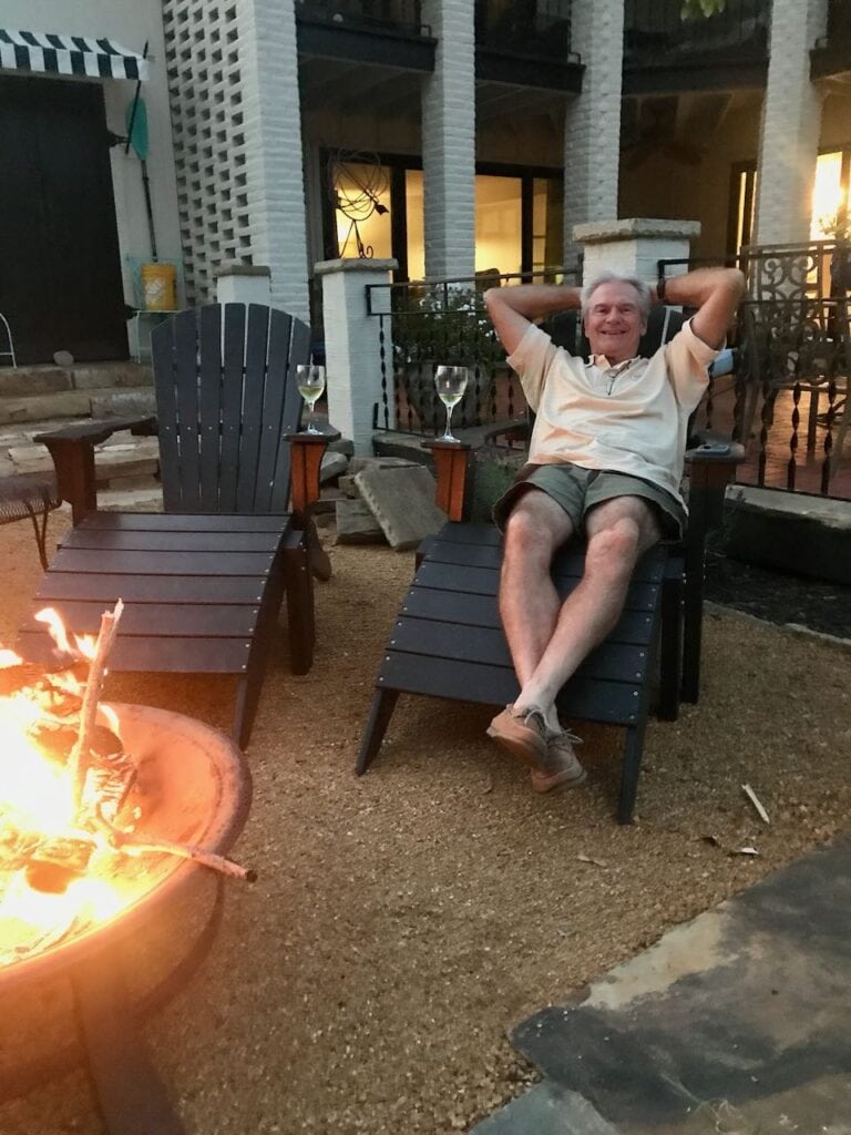 Finished DG patio with a fire burning in a firepit in front of two Adirondack chairs with glasses of wine on the arm rests and a man reclining in one