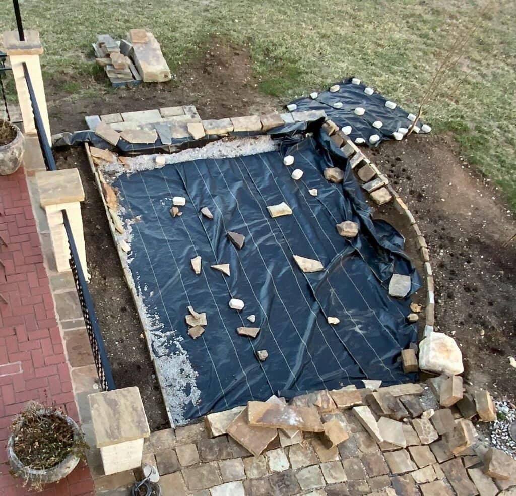 overhead view of new patio area covered in black landscape cloth held down with stones