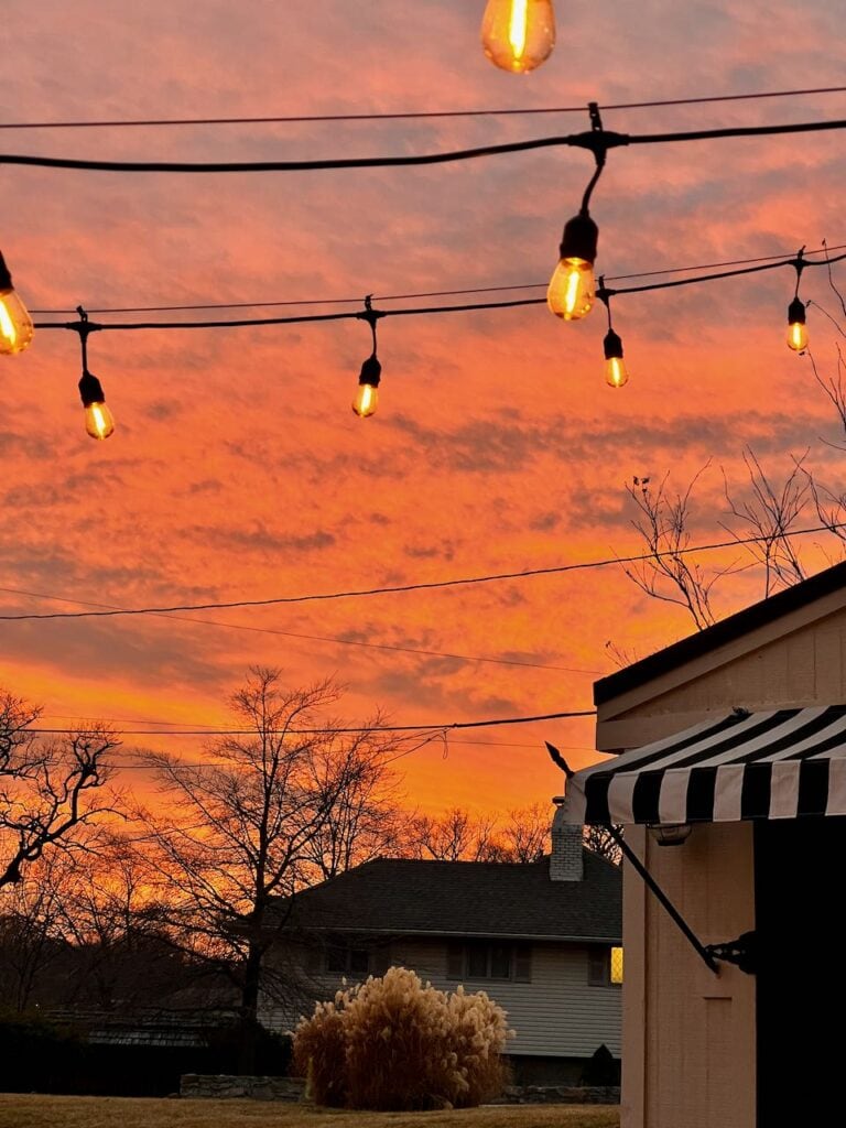 closeup of two strings of edison bulb lights hanging outside with a dramatic sunset behind