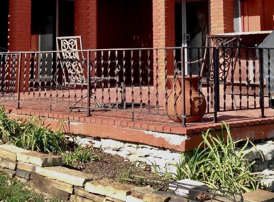 Closeup of a red brick aptio with brlack iron railing around it and the foundation under the outside edge of brick is split and crumbling