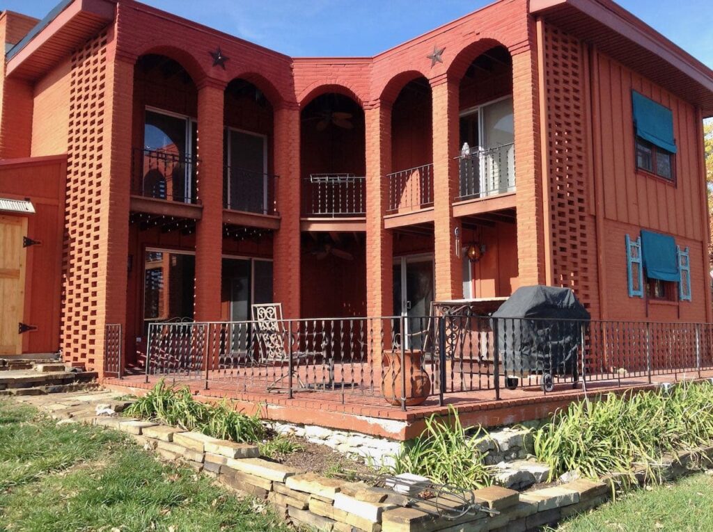 Before picture of the brick patio wrapped on two sides by a 2-story house with 5 large brick arches that shelter the 2nd story balcony