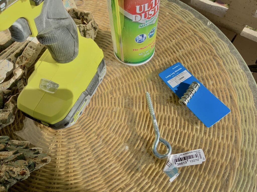 closeup of tools omn a round glass table top. The tools including a Ryobi hammer drill, a can of air, an eyebolt and an anchor