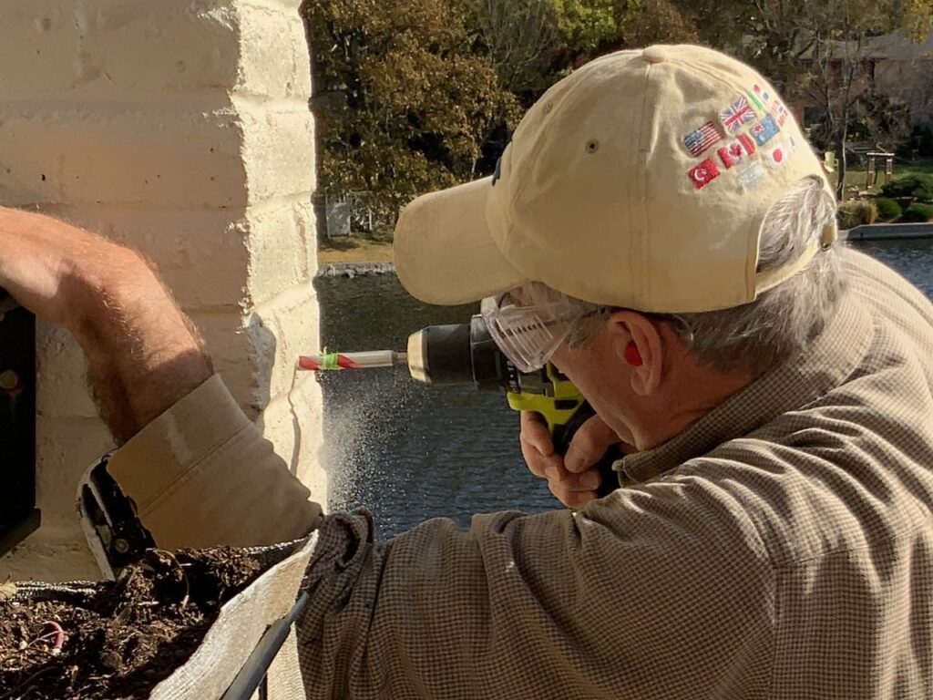 closeup profile of a man wearing a ball hat, safety goggles and ear plugs while drilling into a painted brick column profile