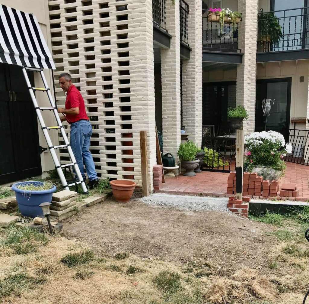 Side view of the Tool Cabana showing how the original stones have been removed and a man is working on installing the awning