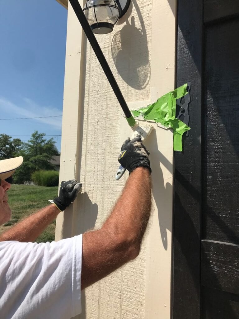 A man's arm is seen as he is painting a block of wood used to support the awning bracket next to the door.