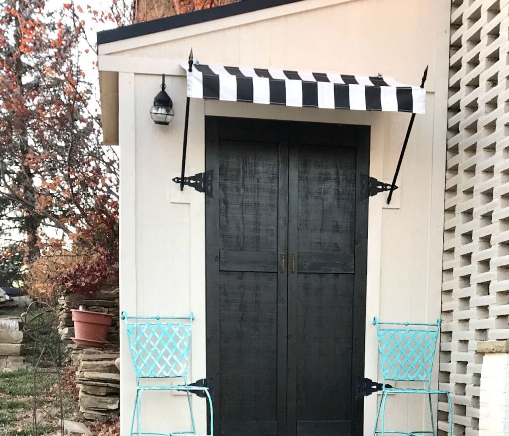 Closeup of tool shed with a cabana stripe awning and new black doors