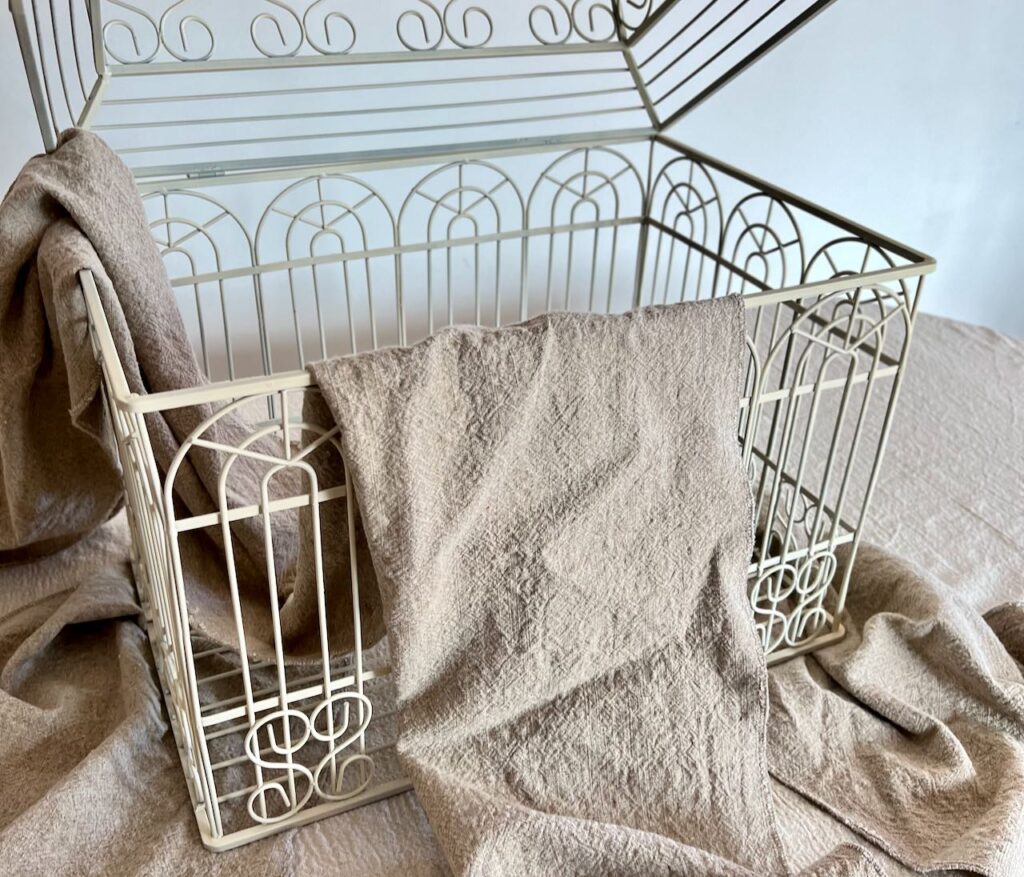 Closeup of a birdcage propped open  with two washed linen table runners, one underneath and the other draped over the side 