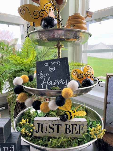 Closeup of a tiered tray overflowing with Bee themed decor focusing on bee-ing kind