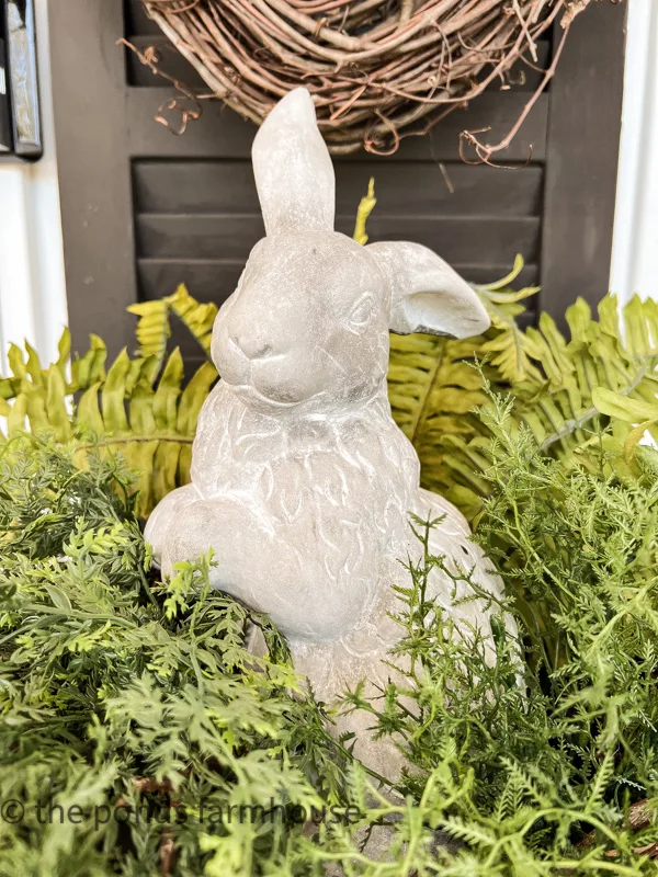 closeup of a concrete bunny statue nestled in amongst greens