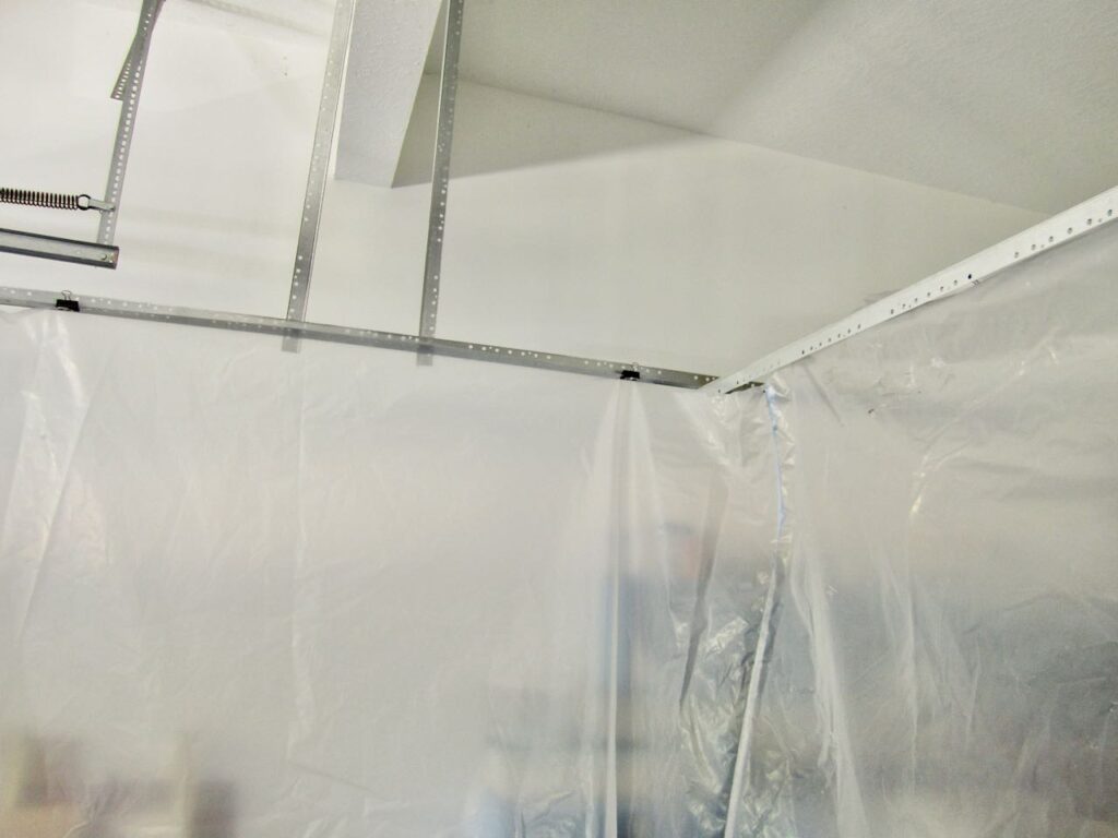 closeup. of the. corner of the paint tent showing the plastic drop cloths suspended from a metal frame with binder clips