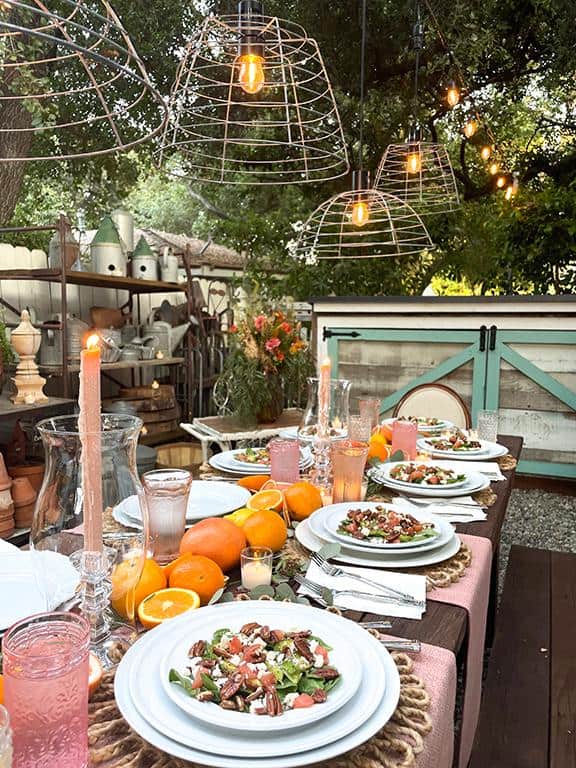 four wire garden baskets with edison light bulbs are suspended over a festive table set in the garden