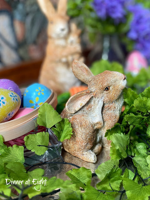Two bunny statues are nestled in faux greens with a few brightly decorated Easter eggs beside them