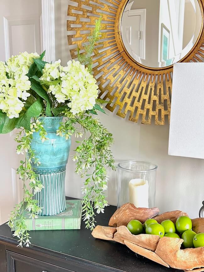 Entry table with a. gorgeous turquoise vase with white hydrangeas and part of a. gold. filigree framed. mirror
