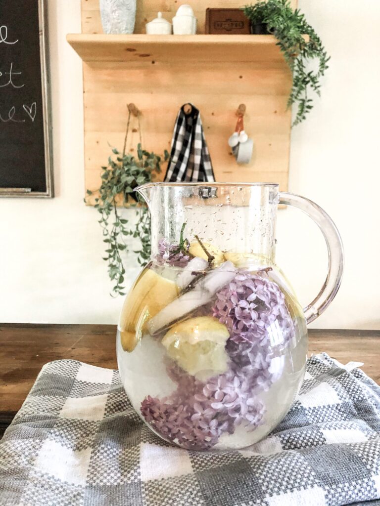 Closeup of clear pitcher with slices oof lemon and lilacs blossoms floating in it