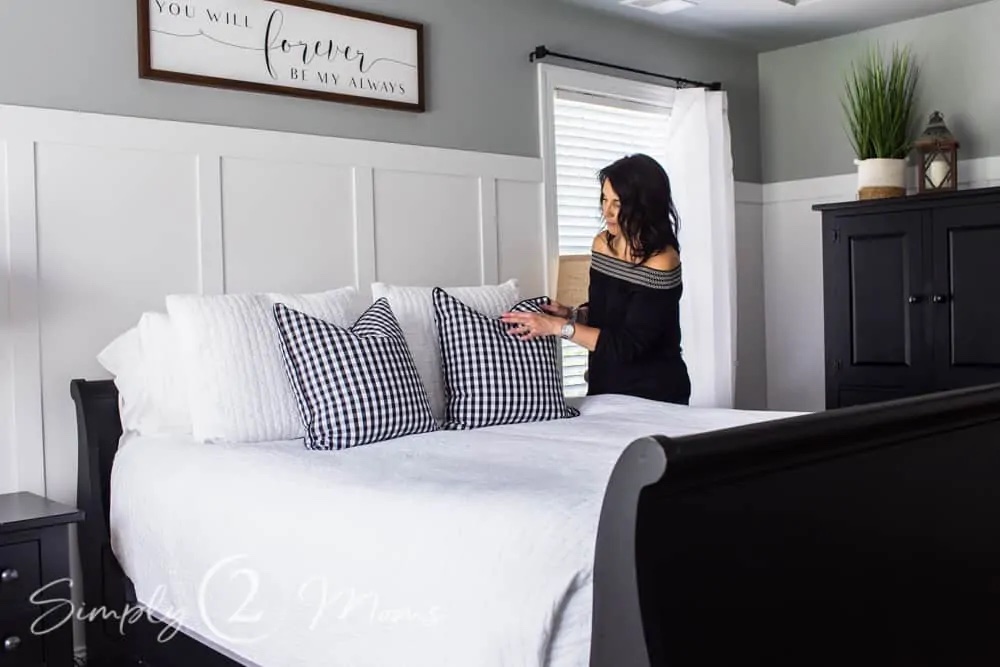 Lady arranging the pillows on a bed in front of an accent wall of board and batten