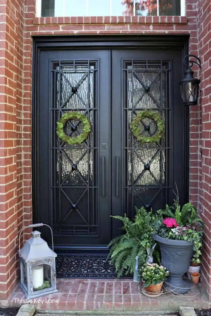 Small red brick porch with a red brick house facade decorateed for Spring with a lantern on one side and a planted urn and bunny statue on the other side