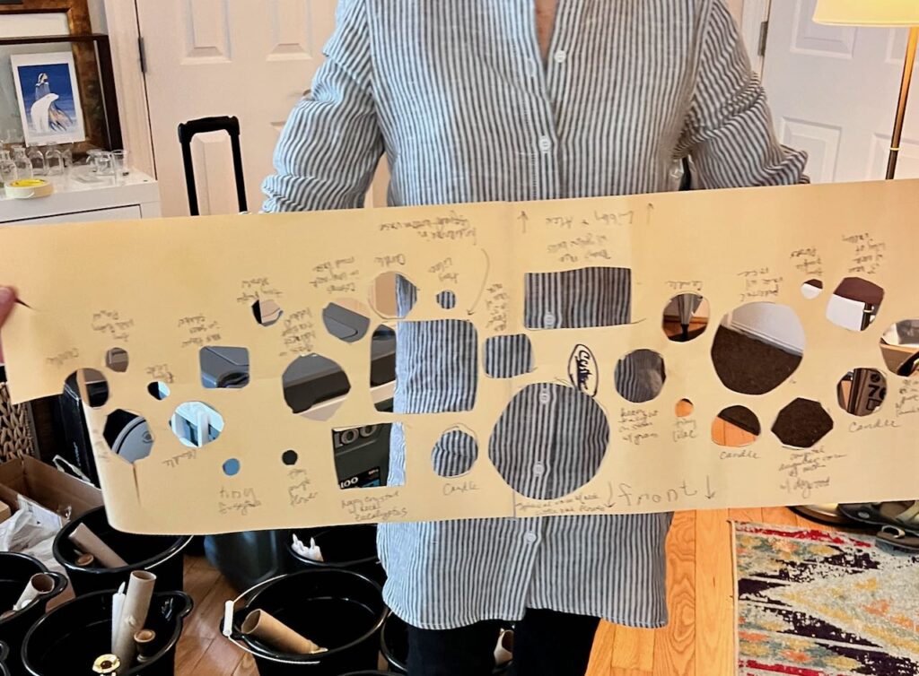 A woman holding the bridal table cluster centerpiece map -- a long piece of paper where the. placement of each vase and flower and each candle has been pre-planned and noted.