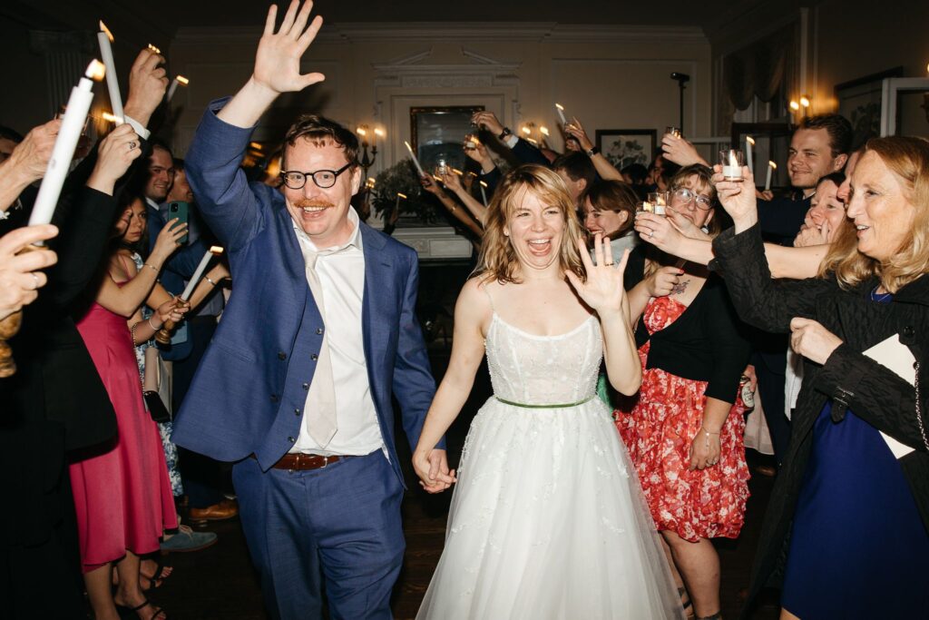 A bride and groom leaving their reception through a tunnel of well-wishers waving and holding up candles