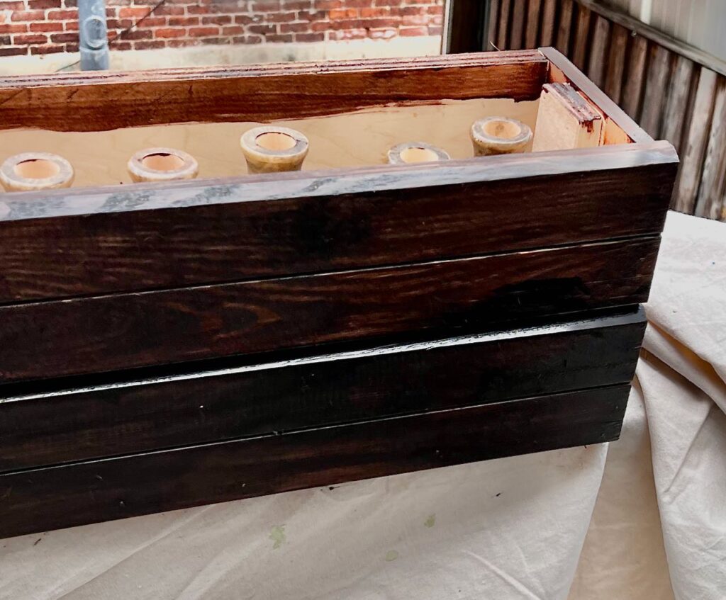 closeup of corner of the long wooden box stained dark, drying on a drop cloth outside