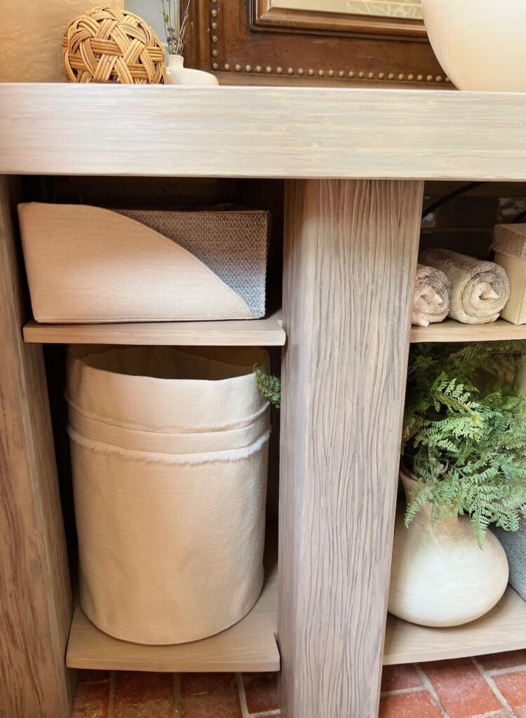 closeup of the finished powder room vanity showing two legs with two shelves showing baskets, bins and rolled towels