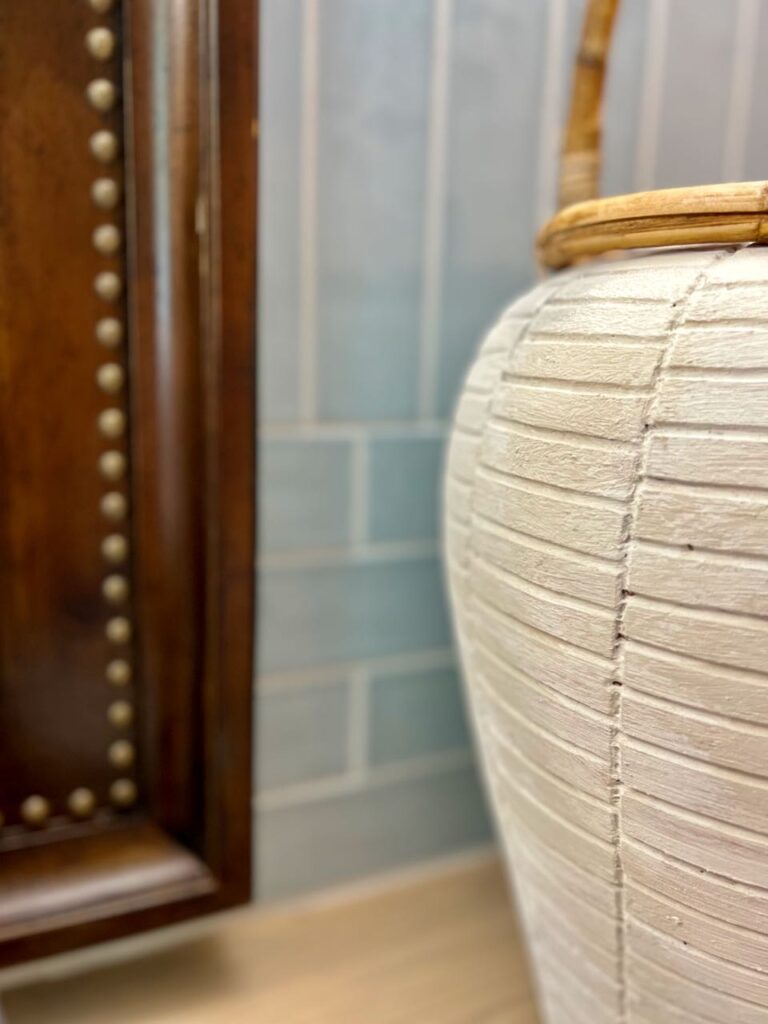 super closeup of large sculpted urn with rattan handle next to wood framed mirror