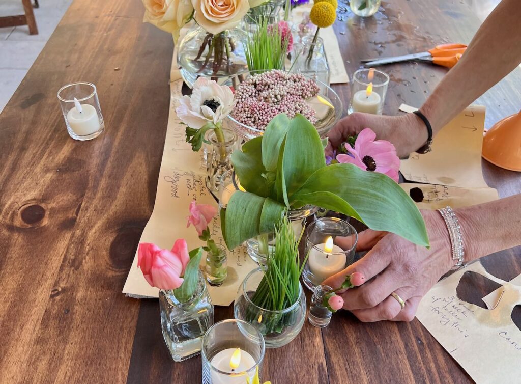 Woman's hands shown cutting the cluster centerpiece map away from the arrangement of vases on the wood bridal table