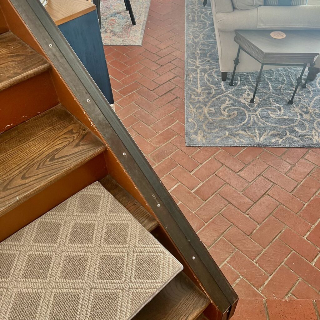 view of diamond carpet sample on the bottom step with the corner of the two downstairs area rugs in the background