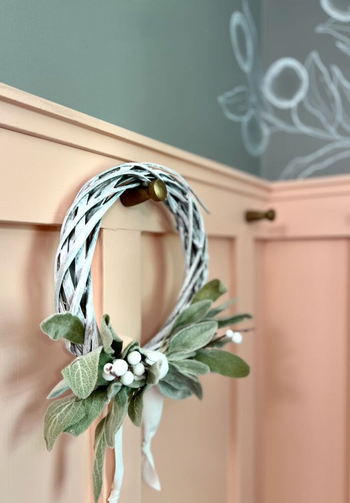 Closeup view of board and batten wall treatment with the old gold pegs and a wreath with dried lambs ear hanging from one of the pegs