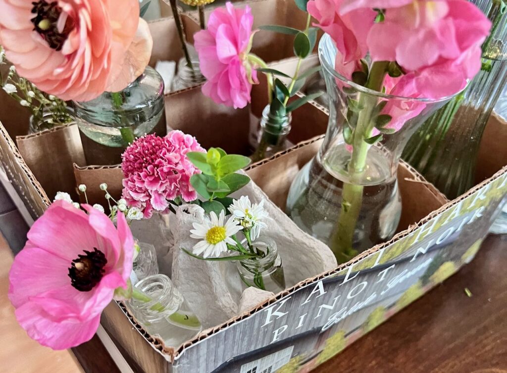 Closeup image of the four=part section of an egg carton nestled in one section of the divided box with all the other bud vases for one cluster wedding centerpiece