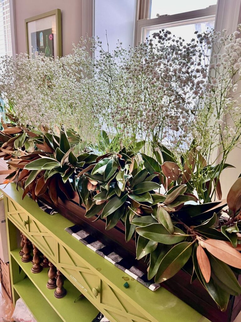 closeup of the dark stained long wooden box filled with fresh magnolia leaves topped with tall wispy branches of Baby's Breath