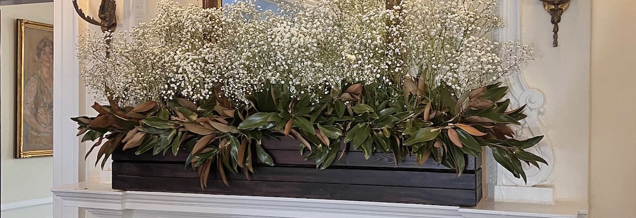 Title Image of dark stained wooden planter box filled with magnolia leaves topped with Baby's Breath on a ornate white mantel