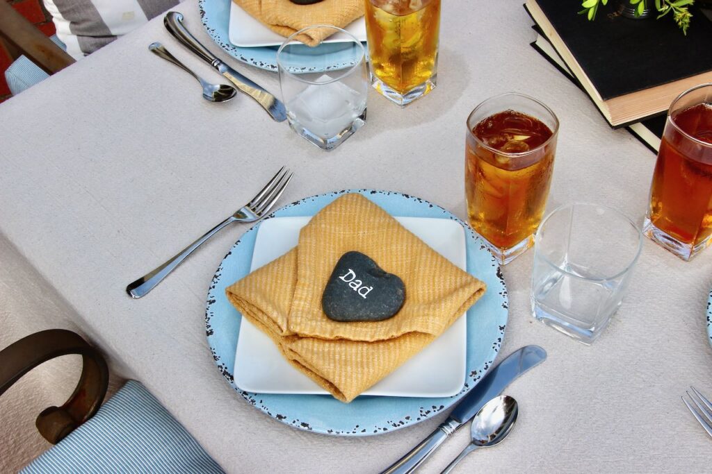 Father's Day Decoration Ideas including a smooth black rock with names in white chalk marker serving as the place card at each placesetting and books as part of the centerpiece