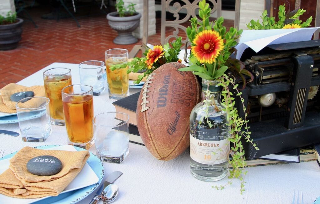 closeup of the Father's Day Decorations featuring a football and an old scotch bottle with flowers and greenery next to the vintage typewriter