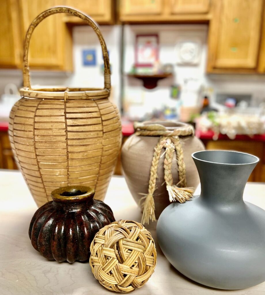 a collection of 4 miss-matched  vessels with a rattan ball sitting together on a work table