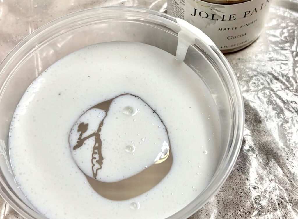 closeup of milky glaze with some dark taupe paint added to it in a plastic to-go container