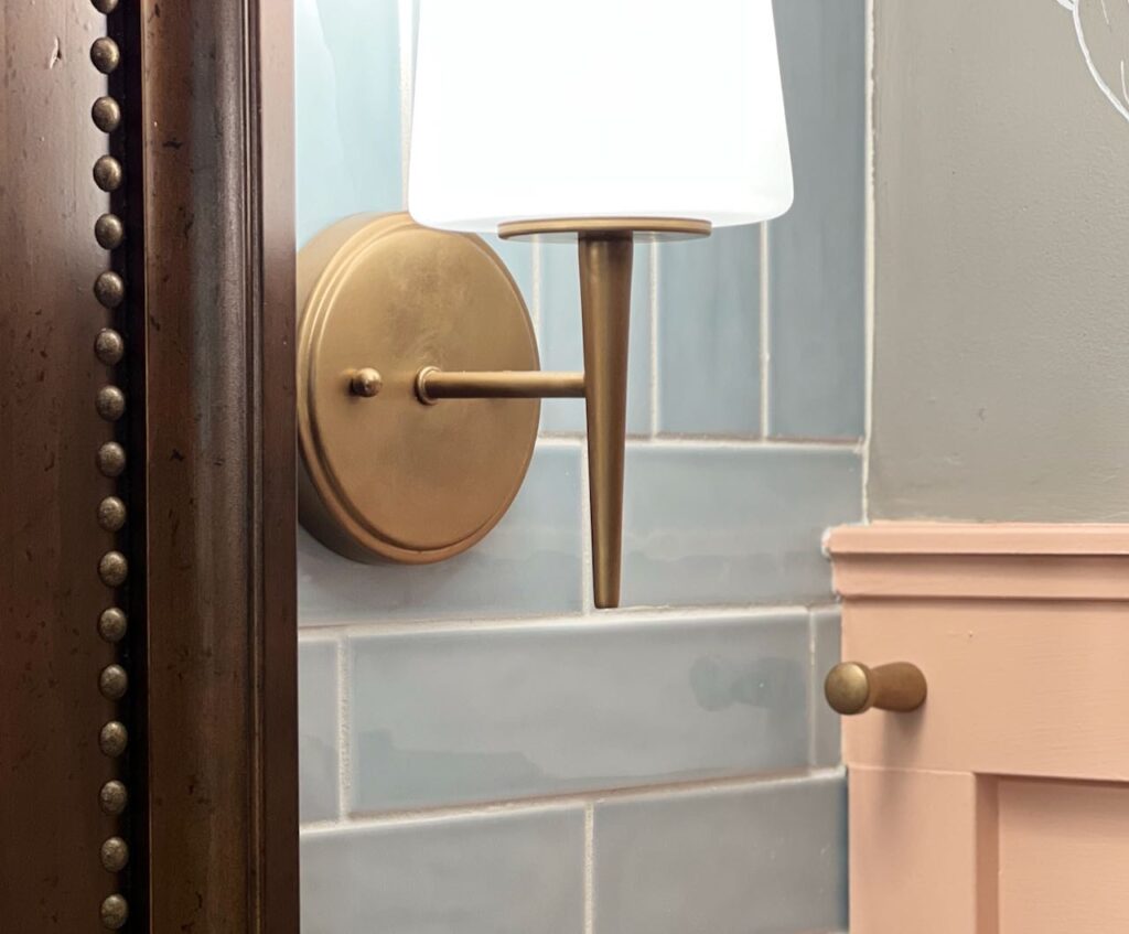 closeup of the gold nailheads on the mirror with the new gold finish of the light fixtures with the gold pegs on the board and batten wall treatment