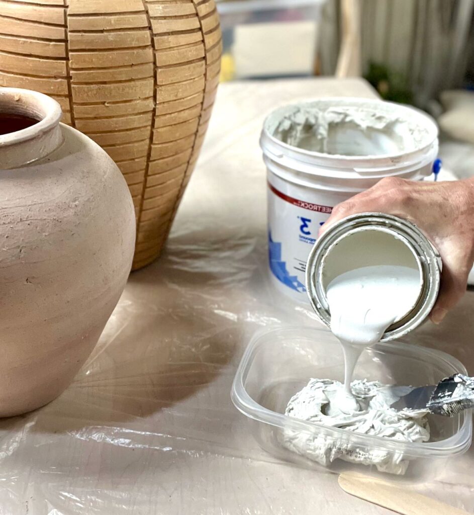 closeup of white chalk paint being poured from a pint size can into a tub of joint compound