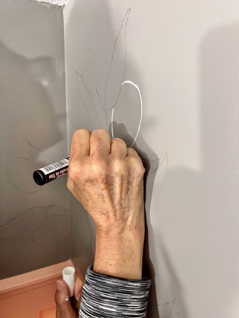 A woman's hand is seen holding a chalk marker and painting over the outline of one of the olives