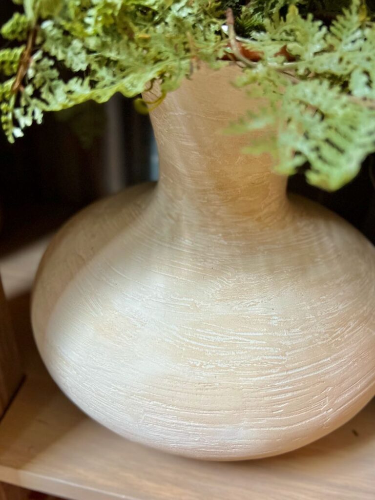 closeup of a madeover vase. on the bottom shelf of the open vanity holding a fern