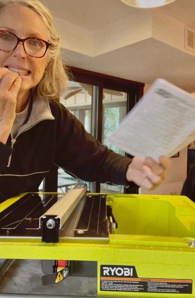 Nervous woman gritting her teeth while leaning over a Ryobi wet saw with a manual in her hand