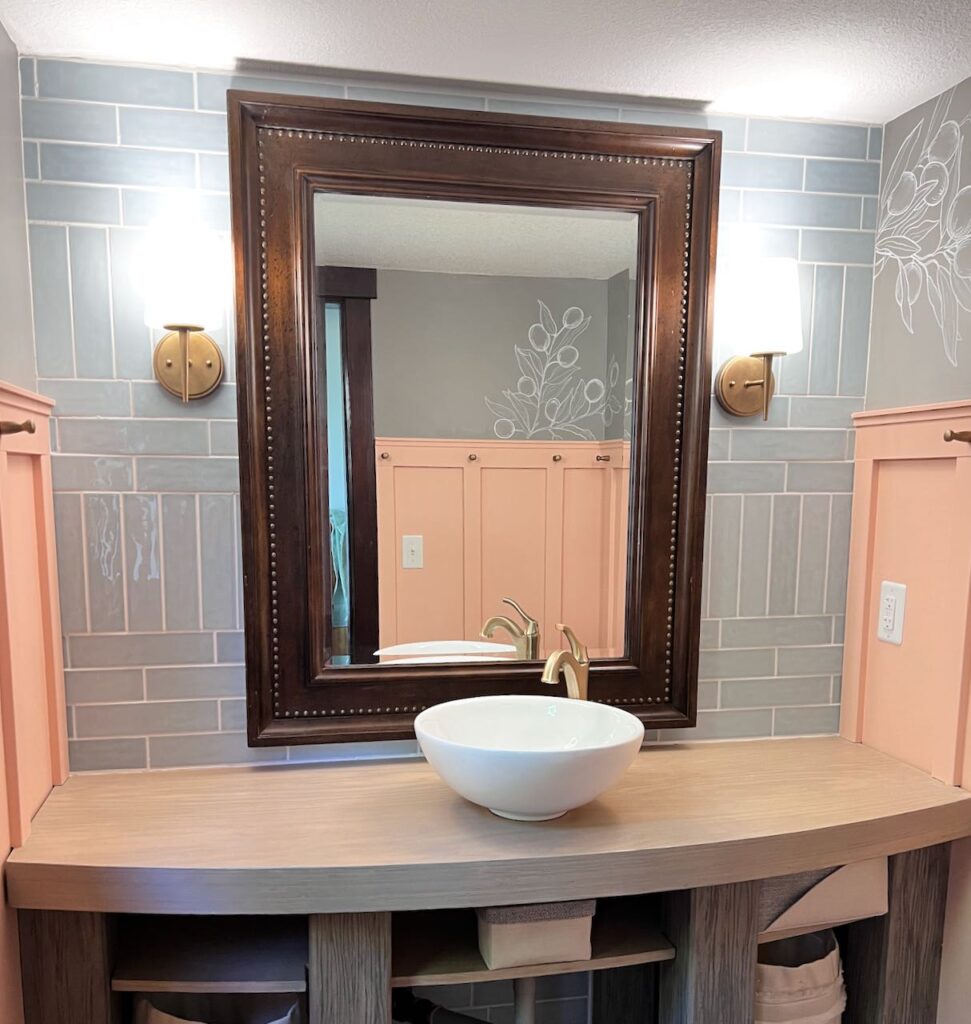 Finished tile accent wall with mirror and lights but no other accessories on the bathroom counter