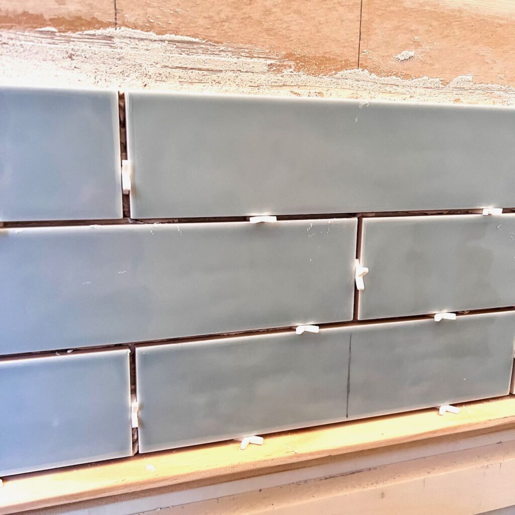 partial wall of tile with white spacers and the spacers between the bottom tiles and a scrap trim board