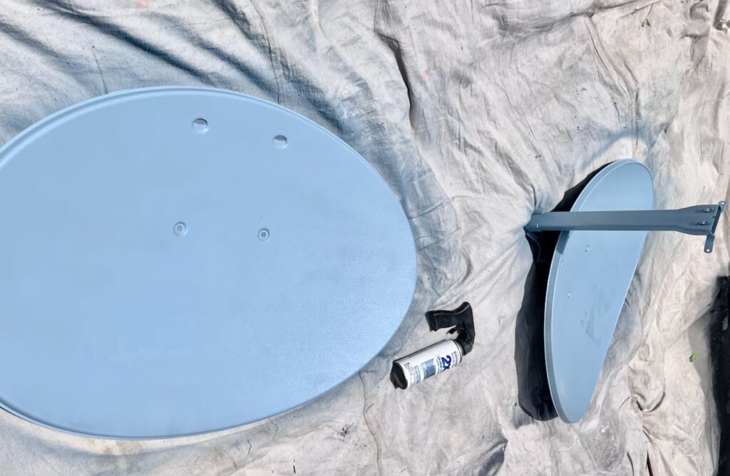 Two repurpose satellite dish are shown on a painter's cloth in the bright sunshine painted blue with a can of Rustoleum spray paint with a trigger grip handle lying between them