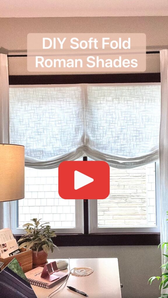 Video play button appears on top of image of office window with soft fold roman shade raised to hide just half the view